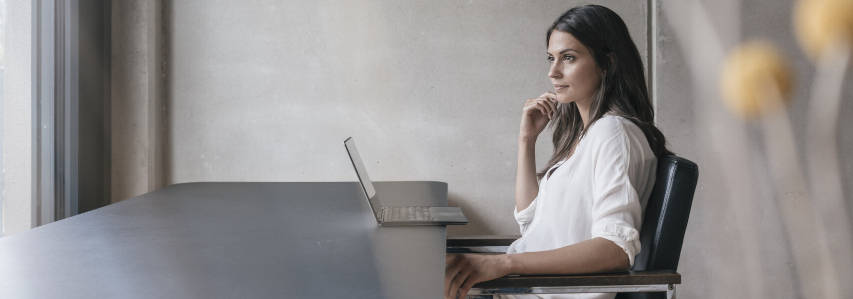 Thoughtful Woman Sitting At Table With Laptop